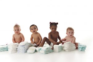 four babies sitting on the floor behind stacks of diapers