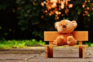 Teddy Bear sitting on a bench outside.